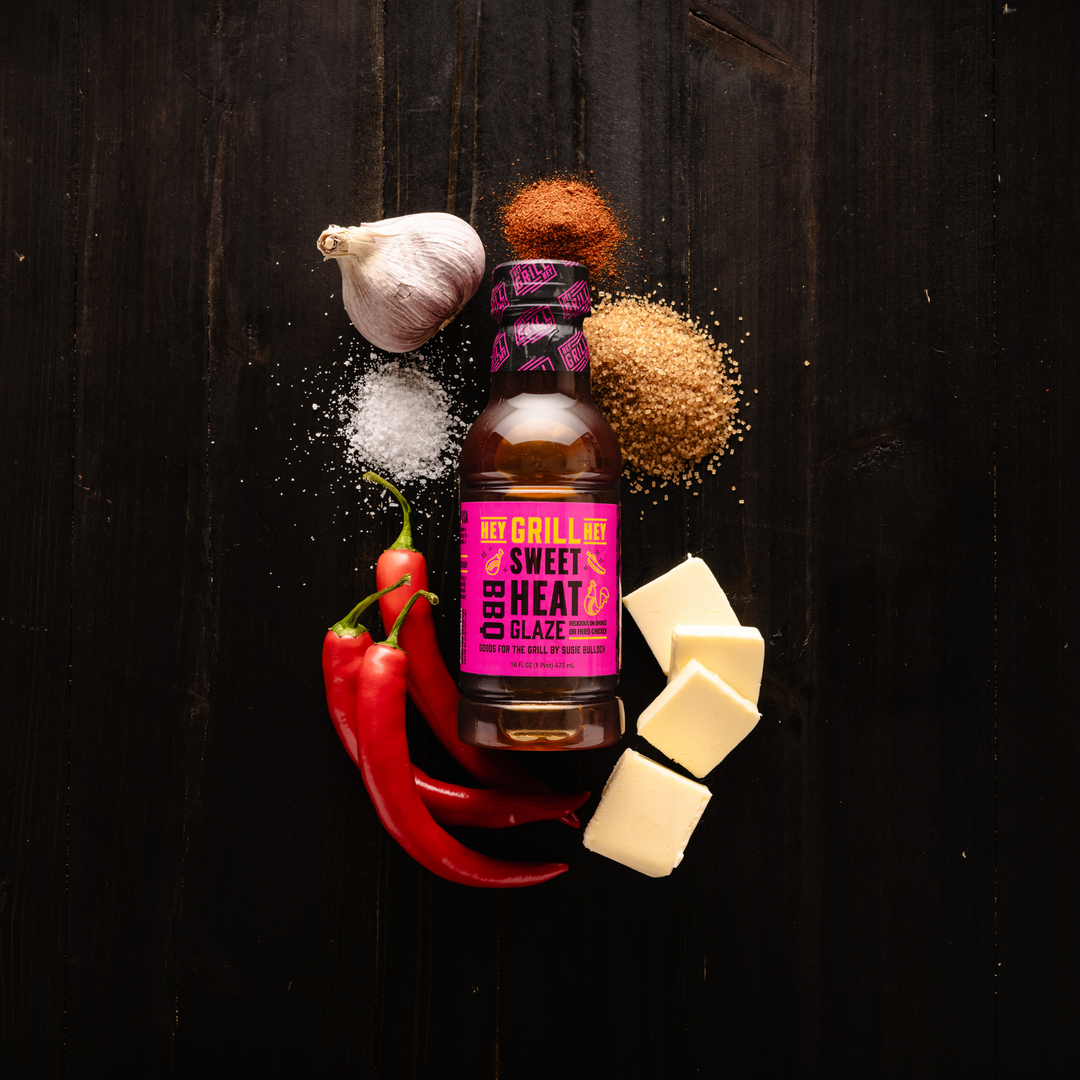 A bottle of Sweet Heat BBQ Glaze surrounded by select ingredients including chili peppers, brown sugar, butter, garlic, and other spices.