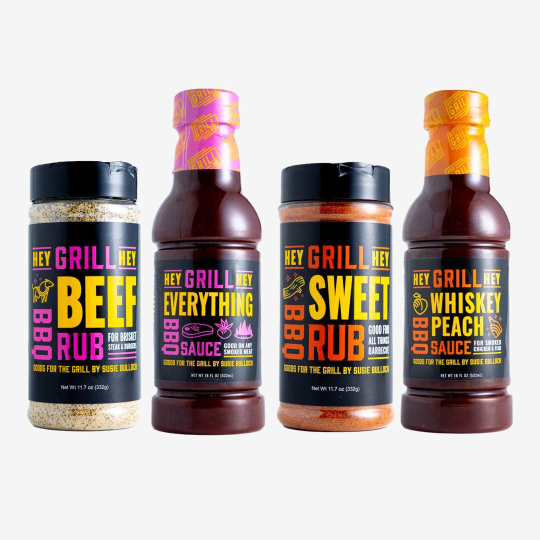 A bottle of Beef Rub, Everythign Sauce, Sweet Rub, and Whiskey Peach Sauce sit on a white background.