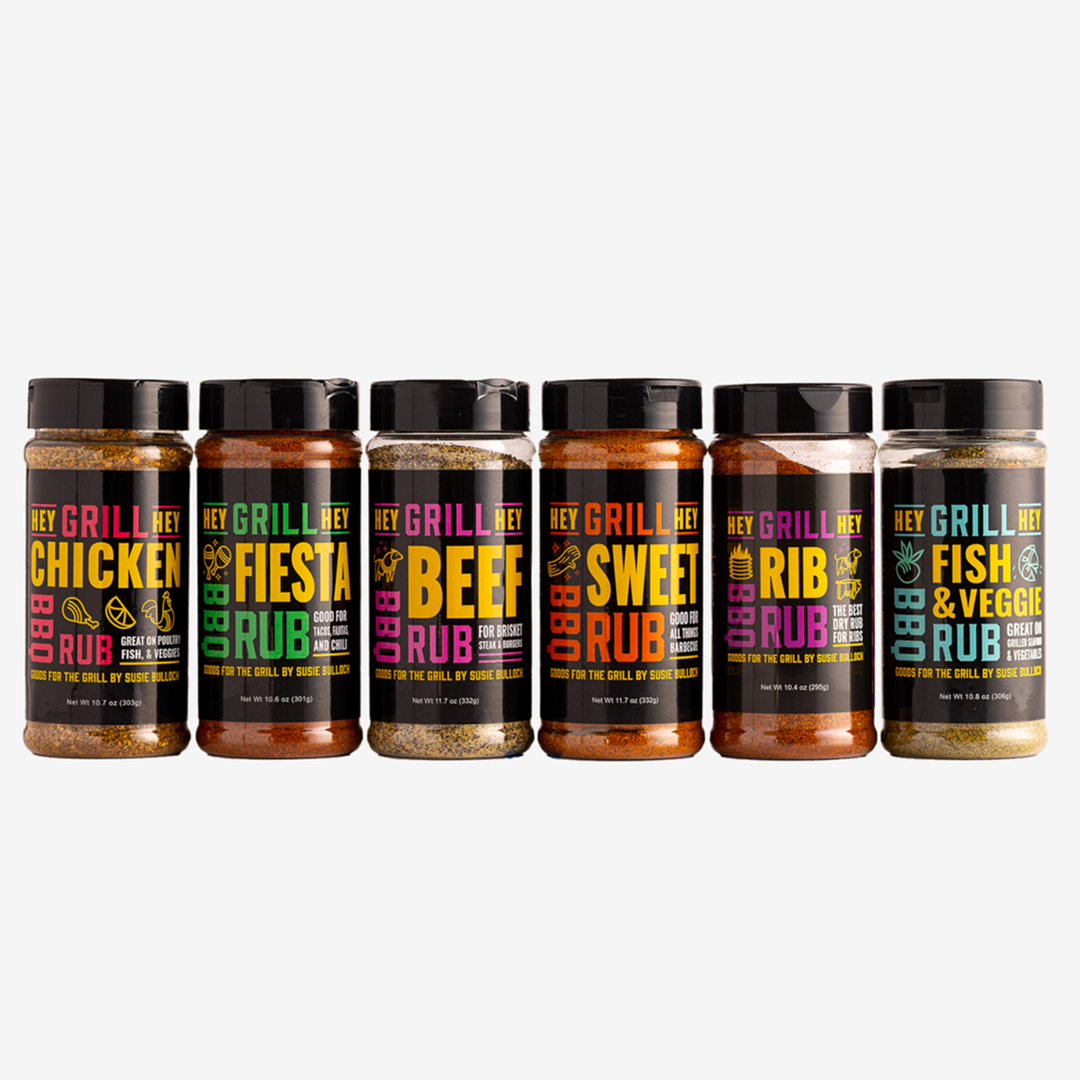 A bottle of Hey Grill Hey Chicken Rub, a bottle of Hey Grill Hey Fiesta Rub, a bottle of Hey Grill Hey Beef Rub, a Bottle of Hey Grill Hey Sweet Rub, a Bottle of Hey Grill Hey Rib Rub, and a bottle of Hey Grill Hey Fish & Veggie Rub all lined up next to each other against a white background.