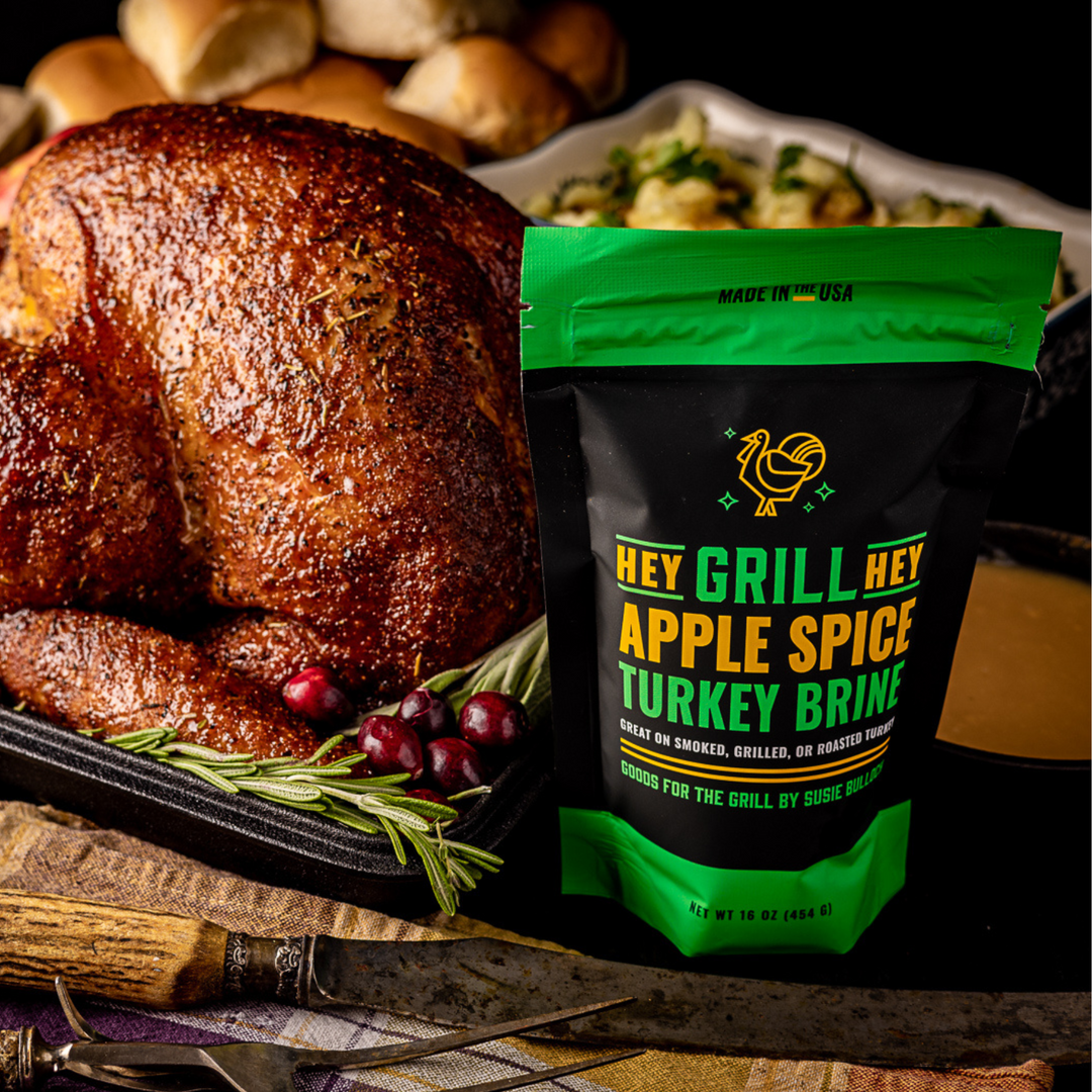 A bag of Hey Grill Hey Apple Spice Turkey Brine placed next to a smoked turkey on a table.