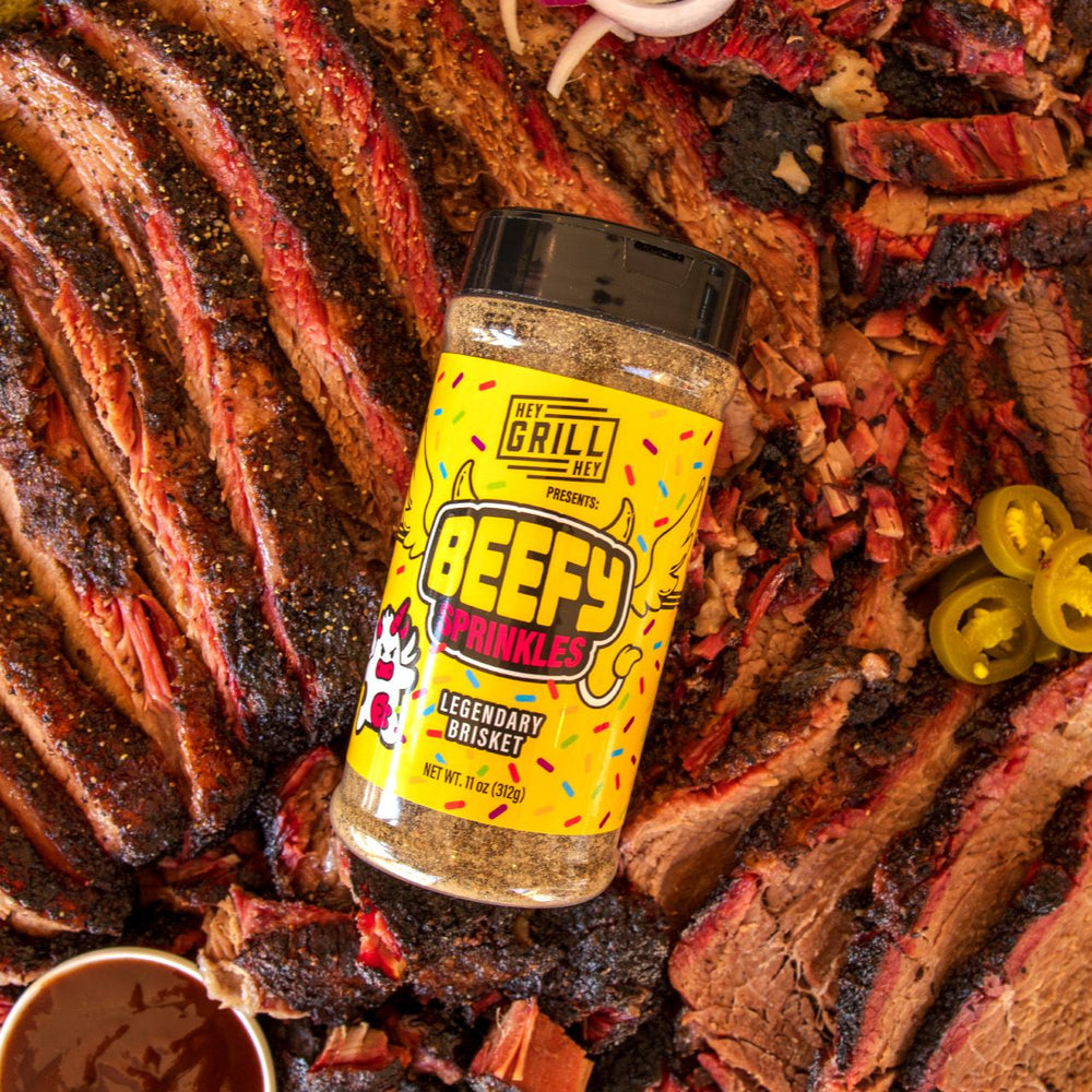 Sliced beef brisket with a bottle of Beefy Sprinkles BBQ Rub on a wooden surface
