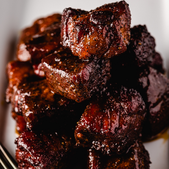 Cooked Pork Belly Burnt ends that were made with Hey Grill Hey Sweet Rub and Hey Grill Hey Everything Sauce, piled high on a white plate.