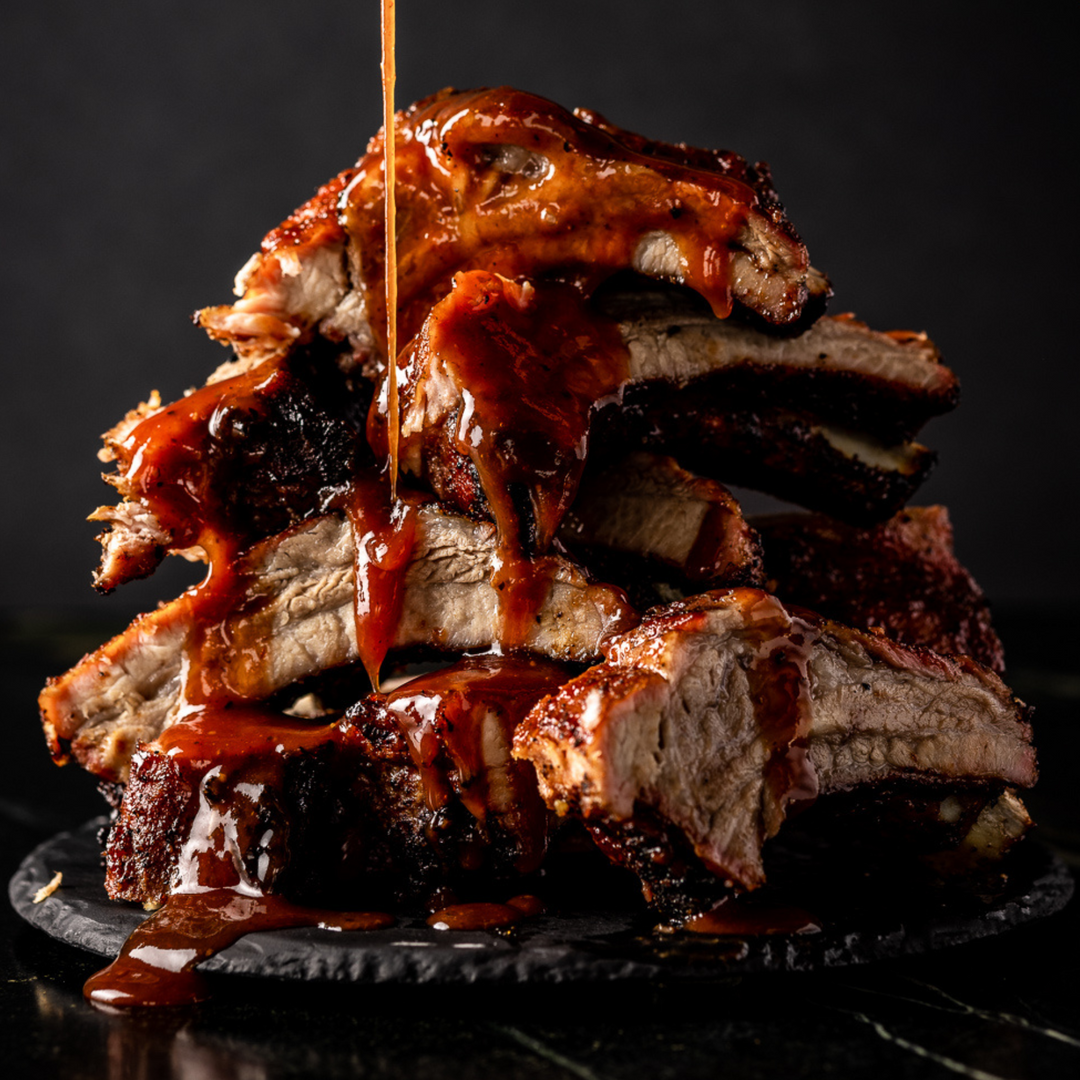 A pile of smoked BBQ ribs are drizzled with Everything BBQ Sauce. 