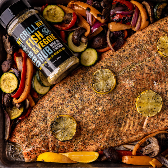 An overhead shot of grilled salmon and vegetables, with a bottle of Hey Grill Hey Fish and Veggie Rub next to it.