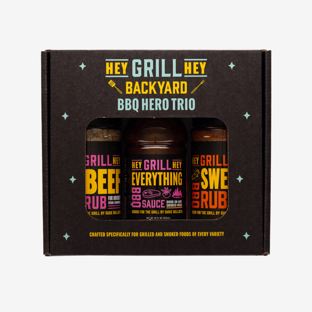 Photo of the front of the Hey Grill Hey Backyard BBQ Hero Trio box. The box reads "Hey Grill Hey Backyard BBQ Hero Trio. Crafted specifically for Grilled and Smoked Foods of Every Variety." and the box contains one bottle of Hey Grill Hey Beef Rub, one bottle of Hey Grill Hey Everything BBQ Sauce, and one bottle of Hey Grill Hey Sweet Rub.