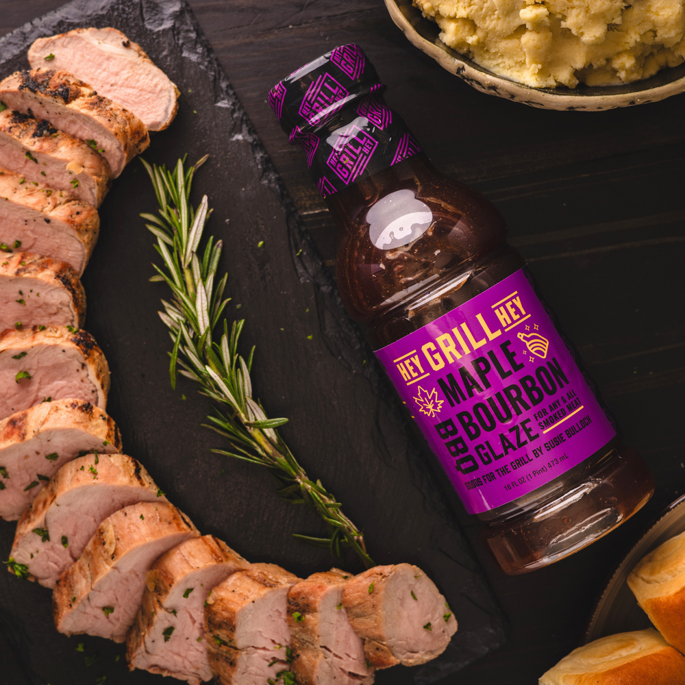 Smoked pork tenderloin is plated and sliced next to a bottle of maple bourbon bbq glaze.  