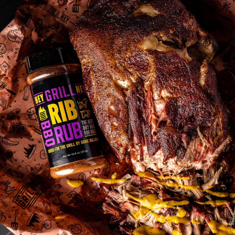 Overhead shot of a smoked pork shoulder with a bottle of Hey Grill Hey Rib Rub lying next to it.