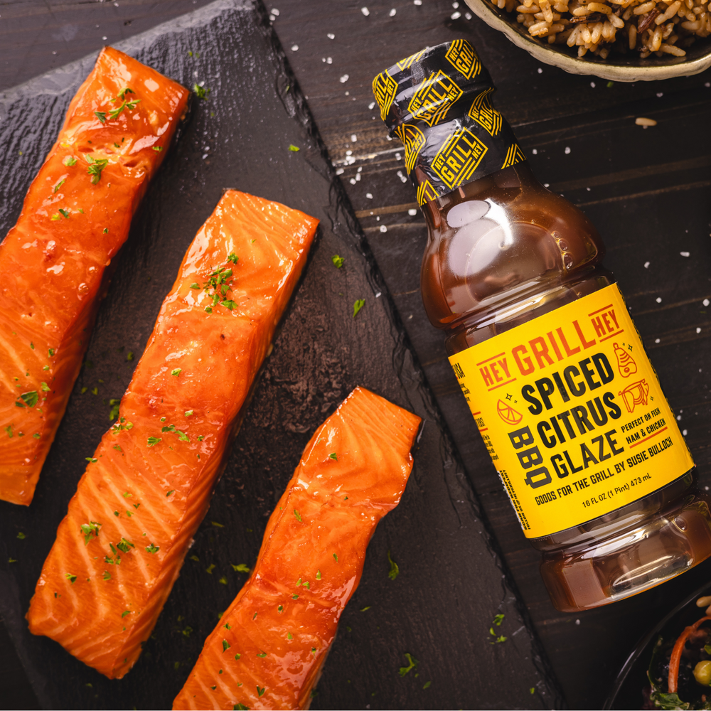 A bottle of Spiced Citrus BBQ Glaze on a table next to freshly glazed salmon. 