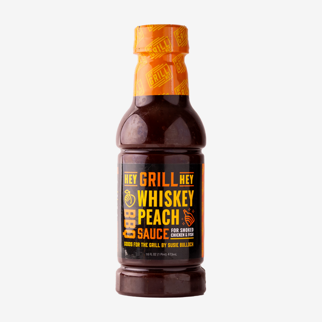 A bottle of Whiskey Peach BBQ Sauce sits on a white background. 