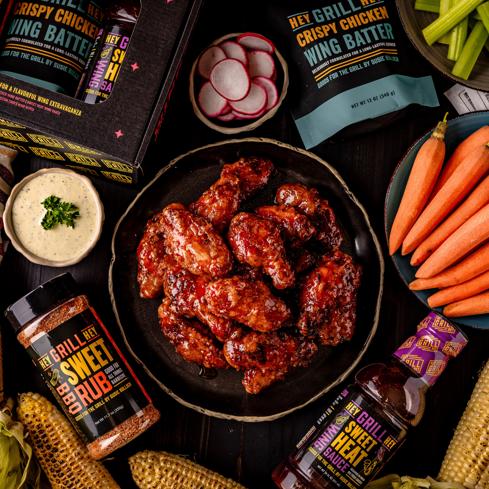 Overhead shot of a plate of smoked & fried chicken wings on a plate. Next to the plate sits a bottle of Hey Grill Hey Sweet Rub, a bottle of Hey Grill Hey Sweet Heat Wing Sauce, and a bag of Hey Grill Hey Crispy Chicken Wing Batter.
