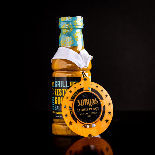 A bottle of Zesty Gold BBQ Sauce sits with a NBBQA Award. 