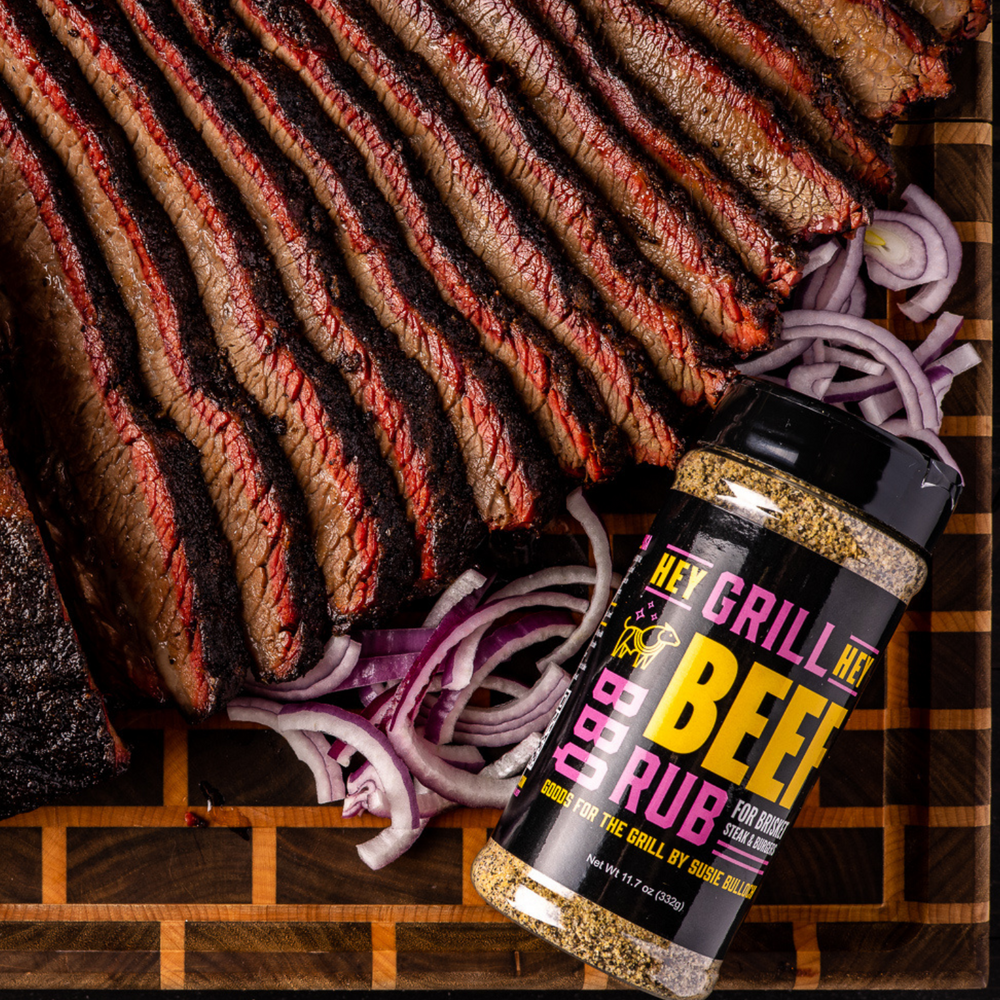 Overhead shot of smoked and sliced brisket on a wooden cutting board with a bottle of Hey Grill Hey Beef rub laying right next to it.