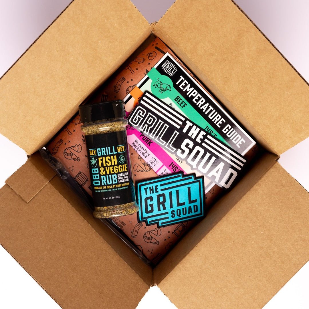 The Grill Squad Welcome Box sits open with a bottle of rub, a Grill Squad Patch, a Grill Squad sticker, and a magnet temperature guide. 